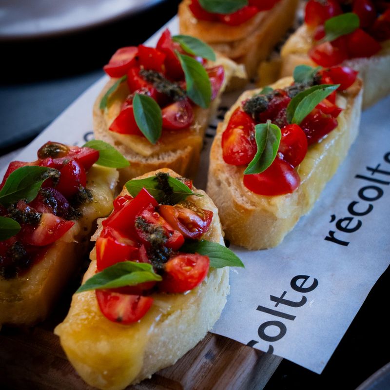 Bruschettas caprese com tomate cereja, queijo derretido, pesto e manjericão