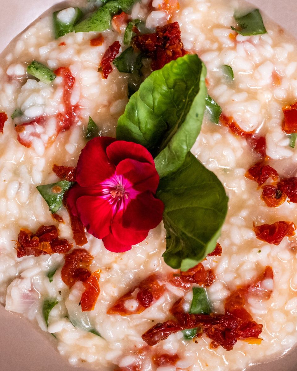 Risoto de tomate seco com folhas de manjericão e uma flor comestível, visto de cima