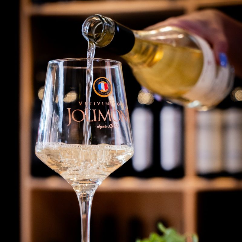 Vinho branco servido numa taça da Jolimont, com a adega ao fundo